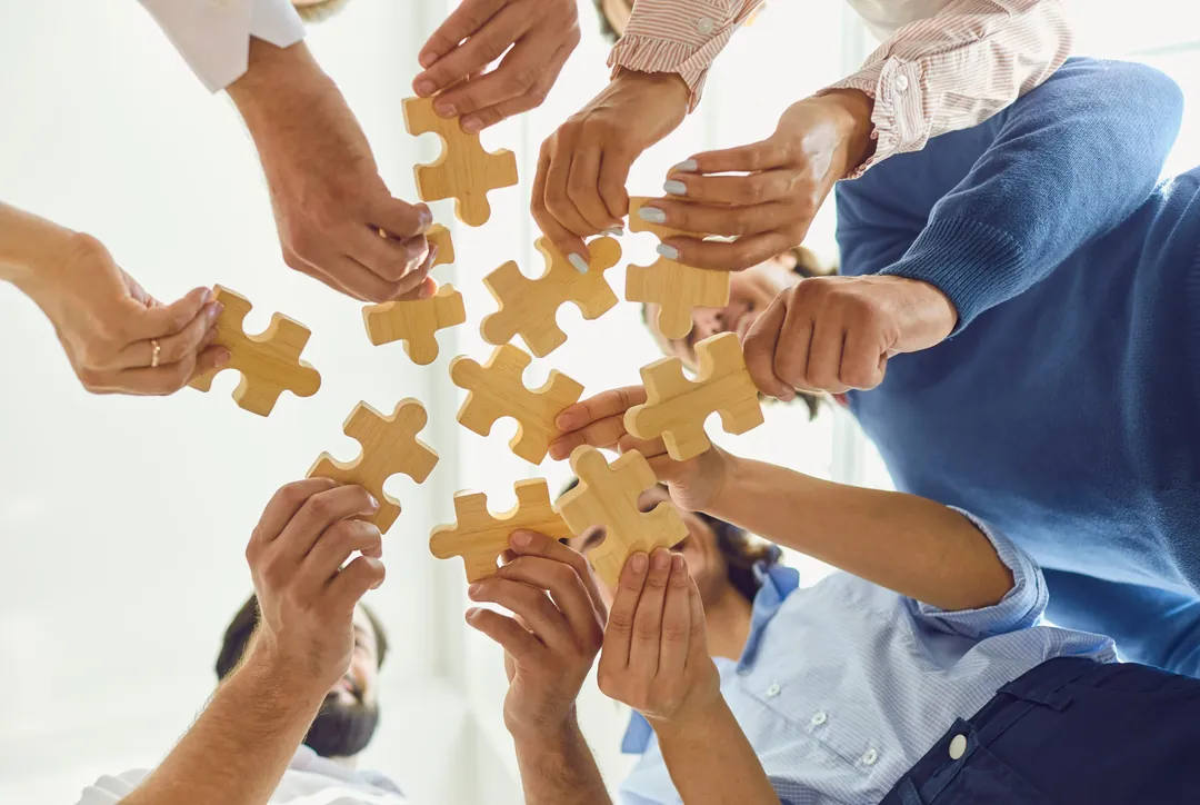 Several pairs of hands fitting puzzle pieces together, representing a collaborative approach to hypnotherapy